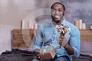 Delighted man holding gift and flowers