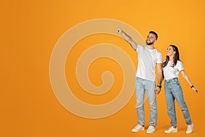 A delighted man and woman in white tops and blue jeans hold hands and point upwards