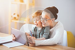 Delighted mother teaching her son using a tablet