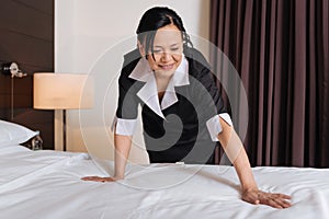 Delighted positive hotel maid cleaning the bed