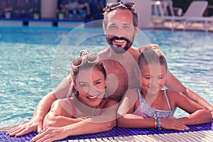 Delighted positive man standing behind his wife and daughter