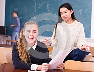 Delighted schoolgirl and Chinese girl schoolmate reading notification photo