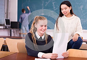 Delighted schoolgirl and Chinese girl schoolmate reading notification photo