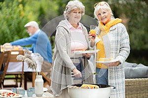 Delighted senior girlfriends with drinks and plates of food