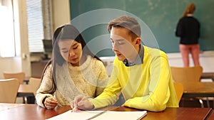 Delighted teenager and Chinese girl schoolmate sitting in classroom, reading notification about approved exams