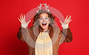 Delighted woman in a Christmas reindeer costume shouts with joy and admiration  on colorful red background