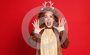 Delighted woman in a Christmas reindeer costume shouts with joy and admiration  on colorful red background