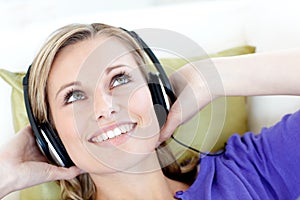 Delighted woman listening to music lying on a sofa