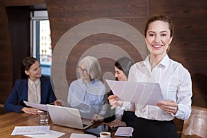 Delighted woman posing in office with documents and colleagues