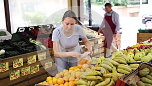 Delighted woman purchaser choosing oranges at the counter in large grocery store