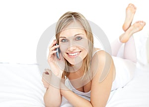 Delighted woman talking on phone lying on her bed