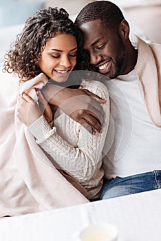 Delighted young African American couple sitting and hugging