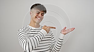 Delighted young hispanic man in stripes, presenting with amazed smile and confident hand gesture, pointing and showing off space