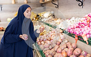 Delighted young Muslim woman purchaser choosing onions in grocery store