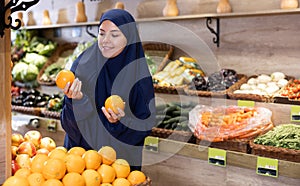 Delighted young Muslim woman purchaser choosing oranges in grocery store