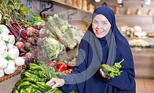 Delighted young Muslim woman purchaser choosing pepper in grocery store