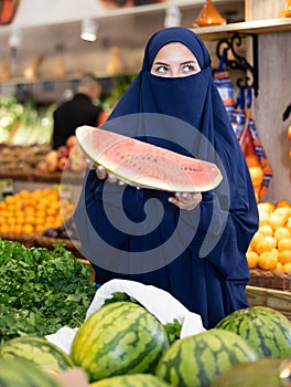Delighted young Muslim woman purchaser choosing watermelon in grocery store