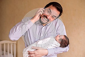 Delighted young parent holding newborn baby daughter and talking on mobile phone. Infant is waiting for attention from father