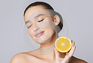 Delighted young pretty woman with closed eyes holding orange half