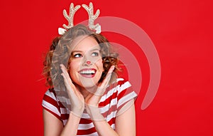 Delighted   young woman in a Christmas reindeer costume laughs and looking up on colorful red background