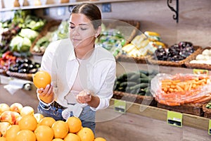 Delighted young woman purchaser choosing oranges in grocery store