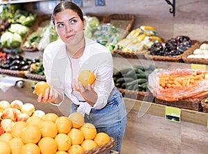 Delighted young woman purchaser choosing oranges in grocery store