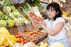 Delighted young woman purchaser choosing tomatoes in grocery store