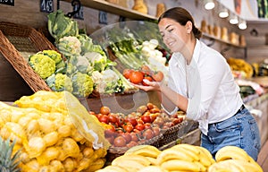Delighted young woman purchaser choosing tomatos in grocery store