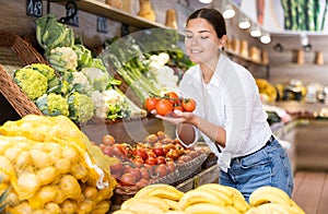 Delighted young woman purchaser choosing tomatos in grocery store