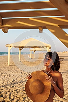 Delightful girl in a hat enjoys her vacation at sea. Happy beautiful young woman smiling on the beach