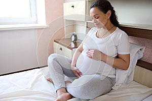 Delightful pregnant woman smiles stroking her belly, feeling connection with her future baby, enjoying his movements