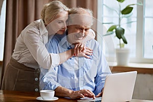 Delightful senior couple, mature man and woman working o laptop at home. Online shopping, communication, paying bills