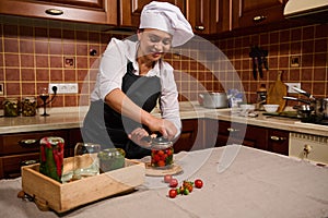 Delightful woman housewife closing lids of jars while canning cherry tomatoes in the home kitchen. Pickling, marinating