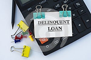 DELINQUENT LOAN - words on a white sheet with clips on a white background with a calculator, buttons and yellow stationery clips