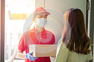 Deliver man wearing face mask in red uniform handing a parcel box over to a customer in front of the house. Postman and express