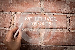 We Deliver Results. Text written with white chalk on a red brick background