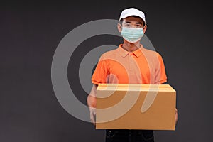Delivery asian man or courier wearing an orange masked uniform holds a cardboard box in the coronavirus concept studio
