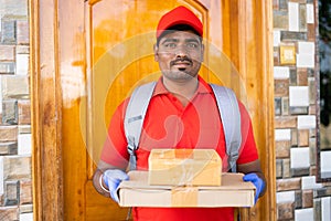 delivery boy with cardboard boxes looking at camera in front of door - concept of small business, Courier service and