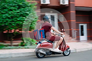 Delivery boy wearing red uniform on scooter with isothermal food case box driving fast. Express food delivery service