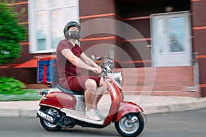 Delivery boy wearing red uniform on scooter with isothermal food case box driving fast. Express food delivery service