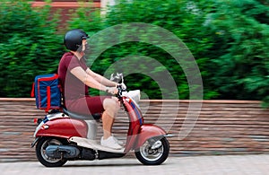 Delivery boy wearing red uniform on scooter with isothermal food case box driving fast. Express food delivery service