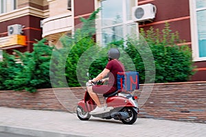 Delivery boy wearing red uniform on scooter with isothermal food case box driving fast. Express food delivery service