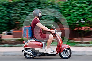 Delivery boy wearing red uniform on scooter with isothermal food case box driving fast. Express food delivery service