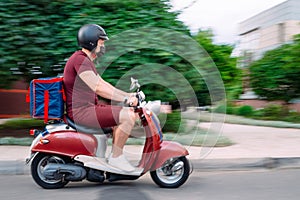 Delivery boy wearing red uniform on scooter with isothermal food case box driving fast. Express food delivery service