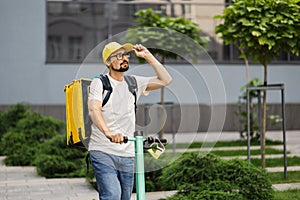 Delivery boy in yellow cap on electic scooter riding on the road.