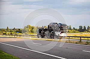 Delivery of cars on a cargo transporter along the highway in the summer. Business in the delivery and sale of cars