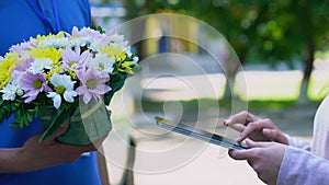 Delivery company client appending signature on tablet and receiving flowers