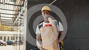 The delivery concept is a beautiful African-American courier standing with a package of food and drinks from the store