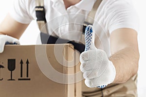 Delivery concept. Courier holds his thumb up. Man with cardboard box close-up. Relocation services. Loader with a box