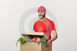 Delivery Concept: Handsome Caucasian grocery delivery courier man in red uniform with grocery box with fresh fruit and